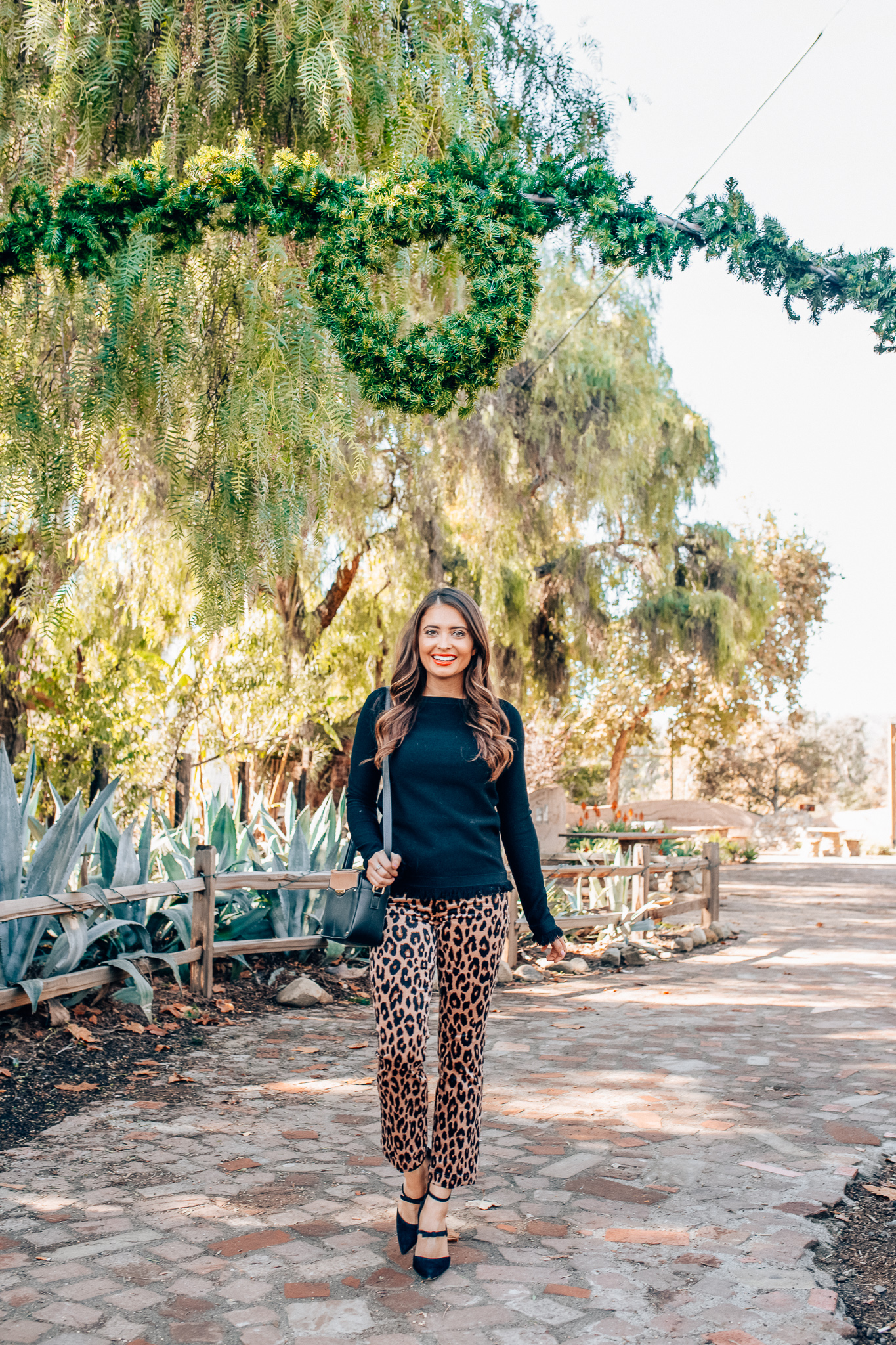 Leopard Holiday style featured by top Orange County fashion blogger, Maxie Elle: image of a woman wearing an Ann Taylor black fringe sweater, Ann Taylor leopard velvet pants, and Ann Taylor camera bag