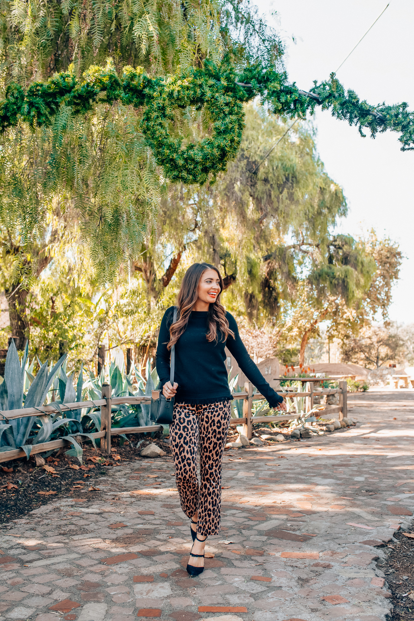 Leopard Holiday style featured by top Orange County fashion blogger, Maxie Elle: image of a woman wearing an Ann Taylor black fringe sweater, Ann Taylor leopard velvet pants, and Ann Taylor camera bag