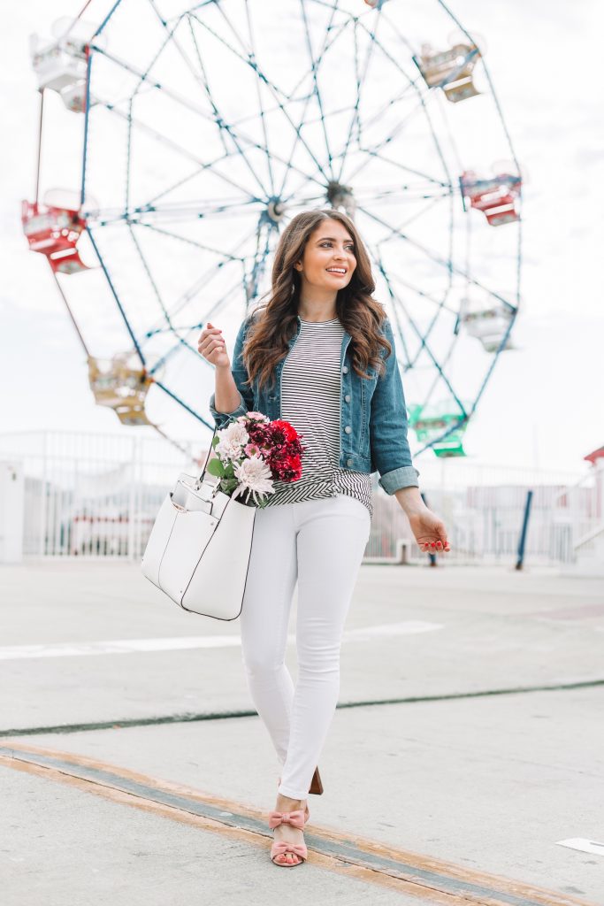 brunette woman in spring jacket and white jeans standing in front of ferris wheel